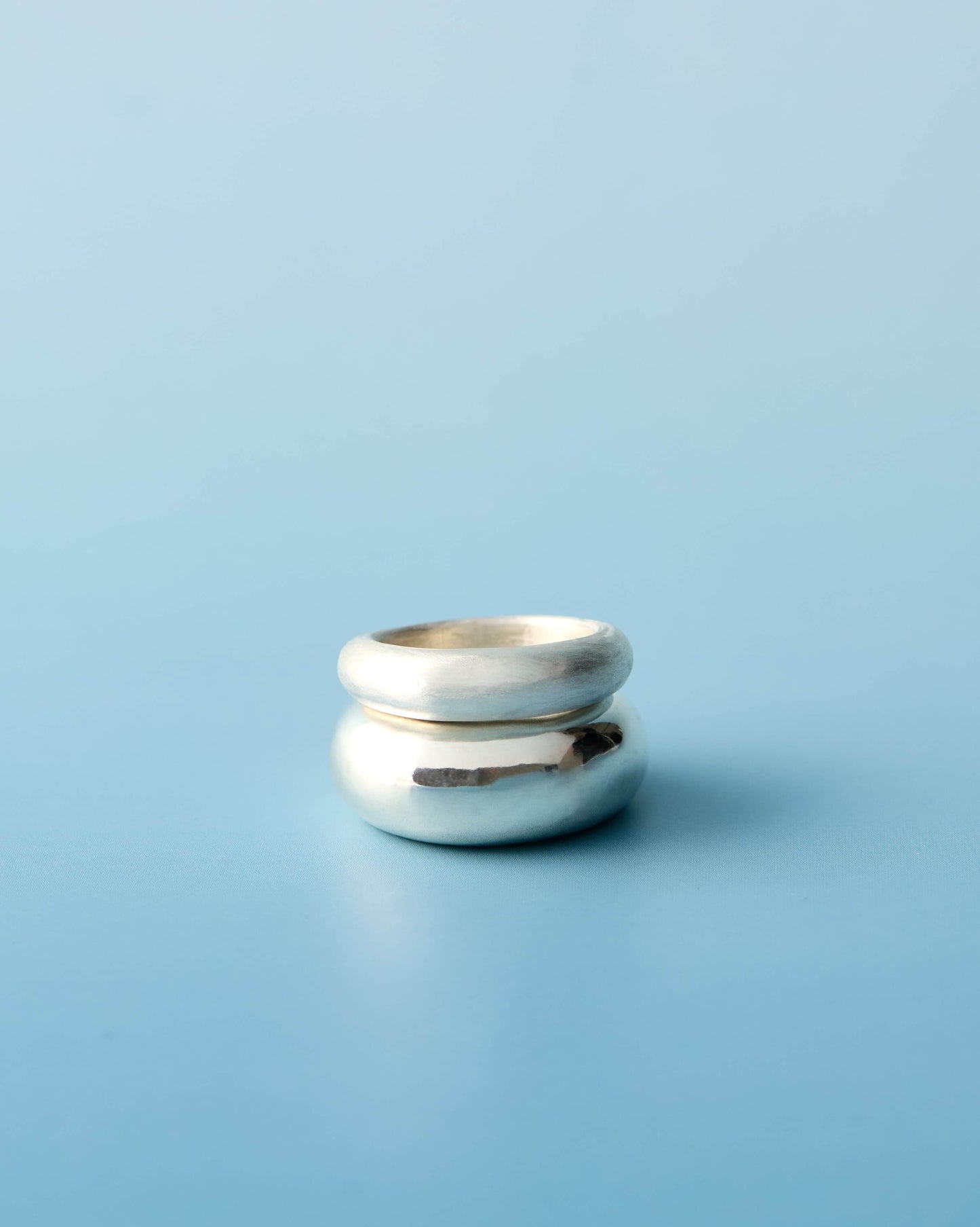 Stacked sterling silver sculptural rings featuring a satin-finish band and a high-polish dome band, photographed on a light blue background. Handmade by LEAP STUDIO.