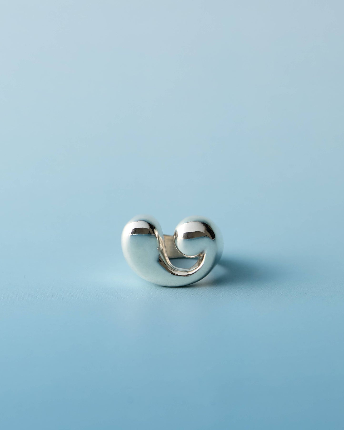 Polished sterling silver sculptural ring with a bold spiral shape, photographed on a light blue background. Handmade by LEAP STUDIO.