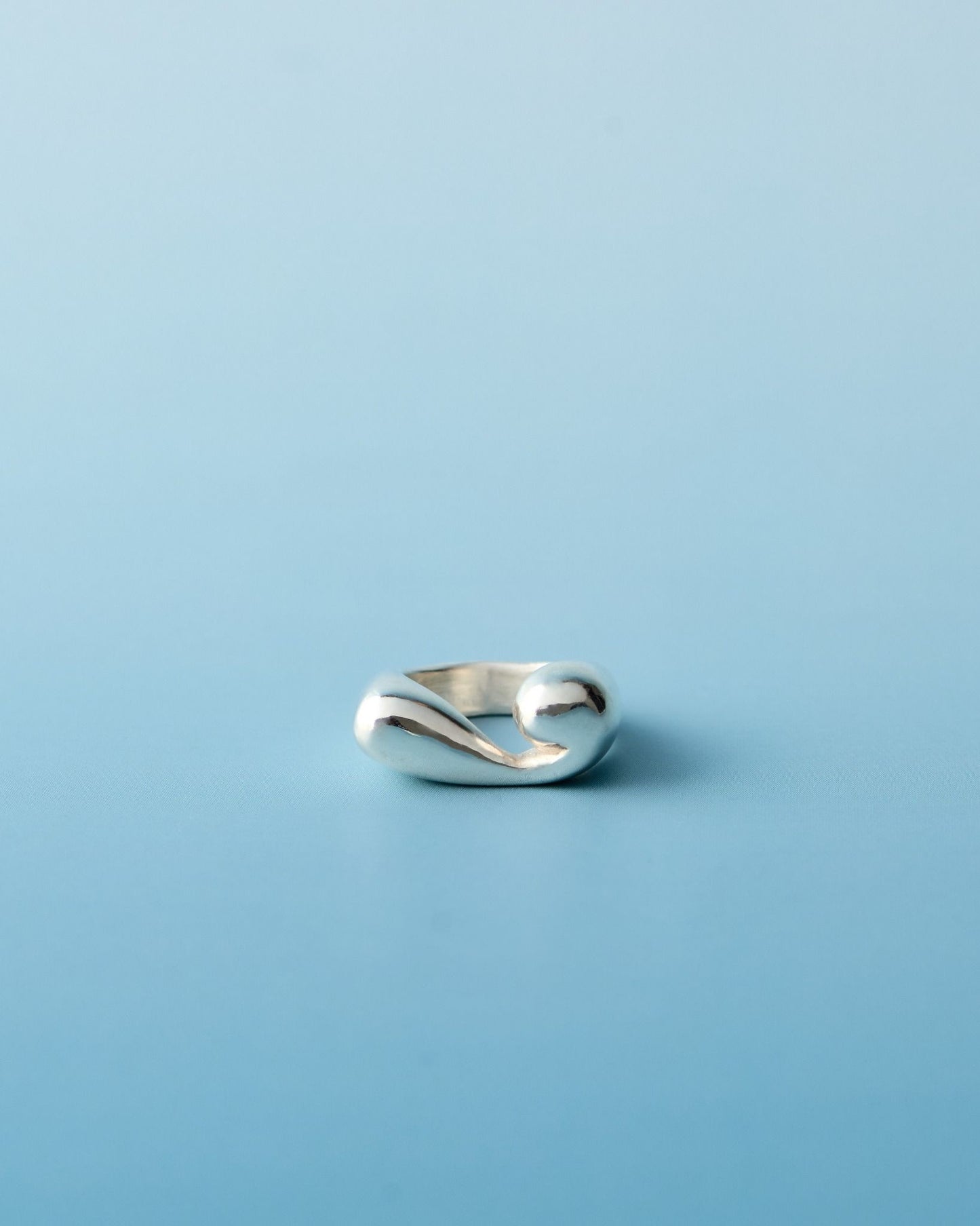 Sterling silver sculptural spiral pinky ring with organic curves, handcrafted by LEAP STUDIO against a soft blue background