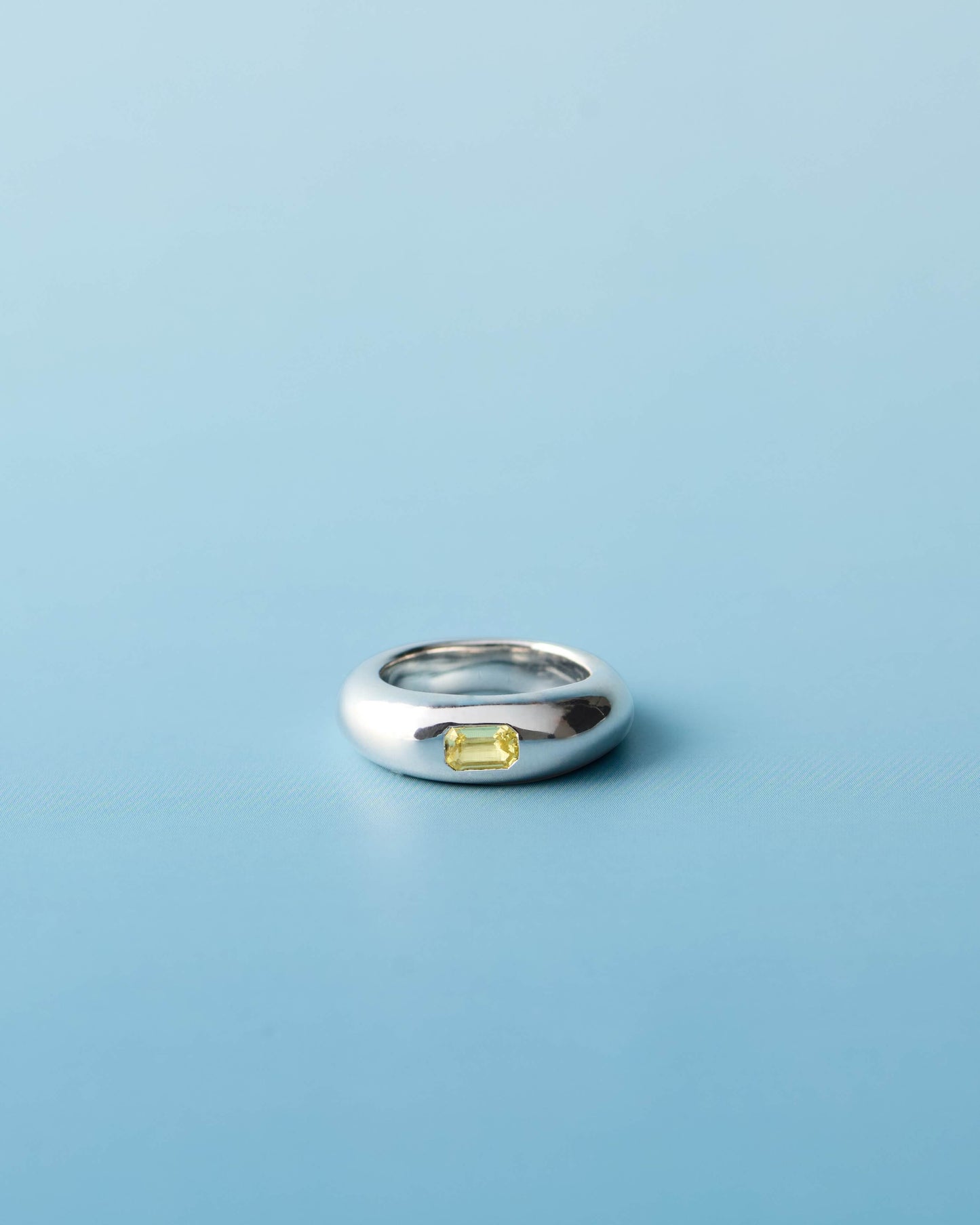 Sterling silver pinky ring with a lab-grown yellow sapphire set on a high-polish dome band, photographed on a light blue background. Handmade by LEAP STUDIO.