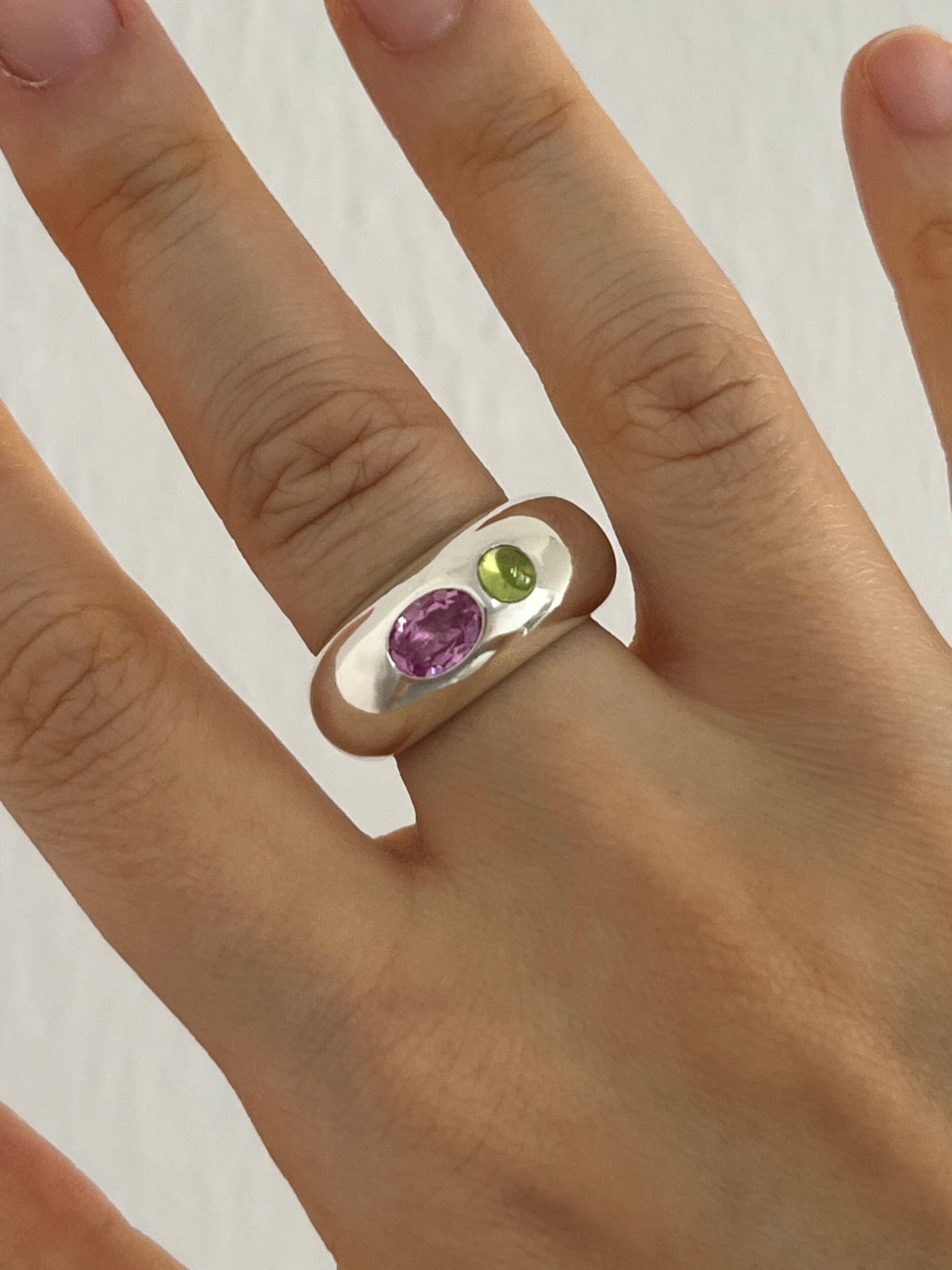 Sterling silver dome ring with a pink oval sapphire and green peridot cabochon, worn on hand. Sculptural, handmade design by LEAP STUDIO showcasing bold color contrast.