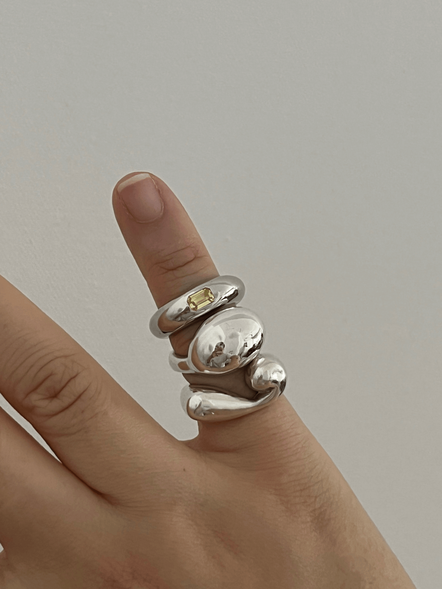 Hand wearing a stacked set of sculptural sterling silver rings, including a yellow sapphire pinky ring and LEAP STUDIO's In Motion Pinky Spiral Ring. Handmade contemporary jewelry.