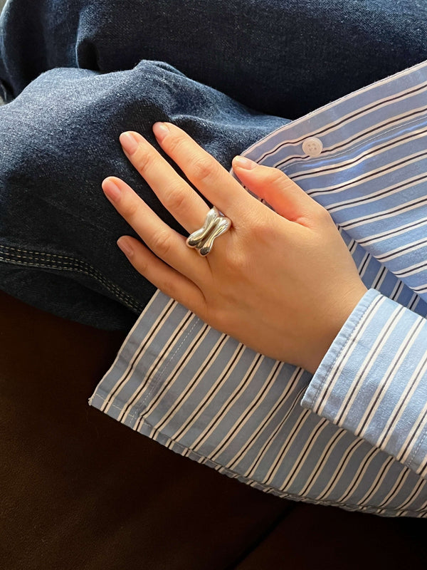 Handmade sculptural Silver Lining ring in polished silver, featuring soft curves and a central slit that reveals a glimpse of skin. Worn on a hand resting on denim, paired with a blue and white striped shirt, the ring’s organic shape and reflective surface are subtly emphasized.