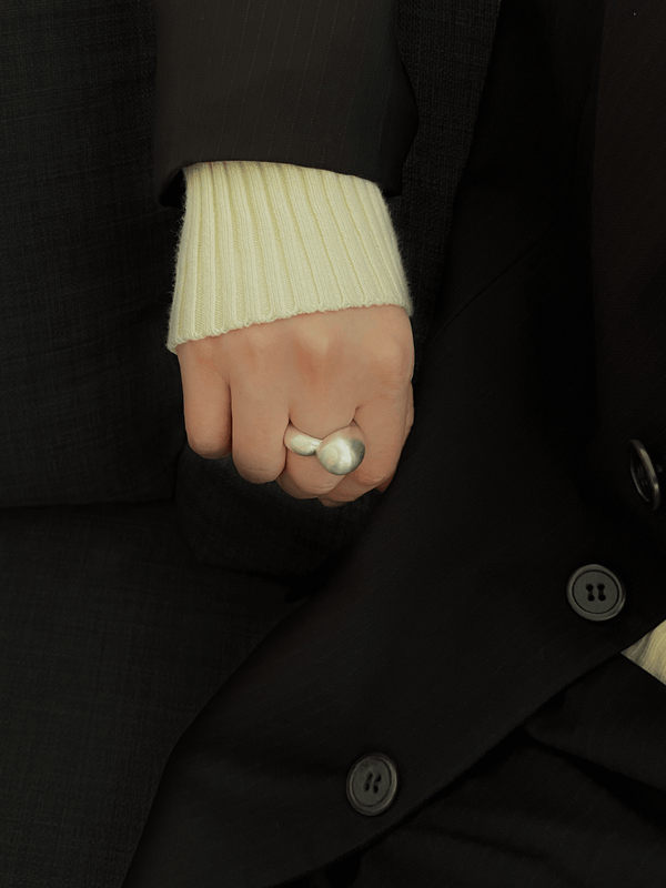 Chunky handmade silver ring with flowing, sculptural lines, worn on a hand in soft daylight. The design wraps naturally around the finger, emphasizing its fluid shape.